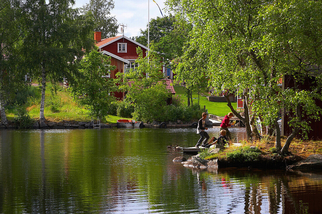 Holzhaus und am Wasser spielende Kinder in Sundborn, Dalarna, Mittelschweden