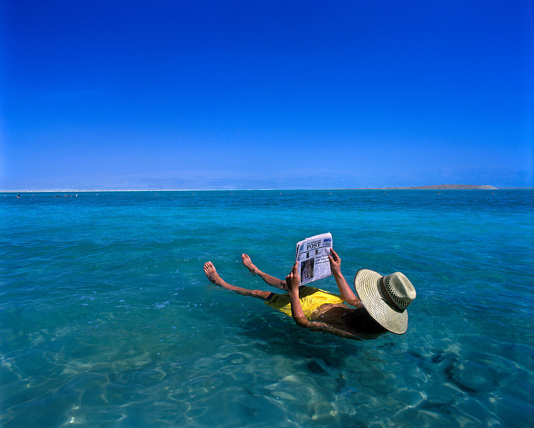Floating man reading newspaper, Ein bokek, Dead sea, Israel.