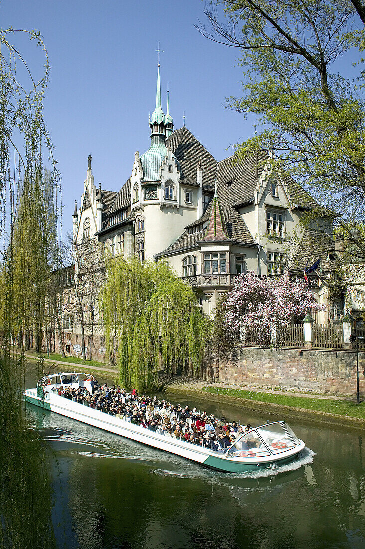 Tourist boat on Ill river and Lycée des Pontonniers International high school in springtime. Strasbourg. Alsace. France.
