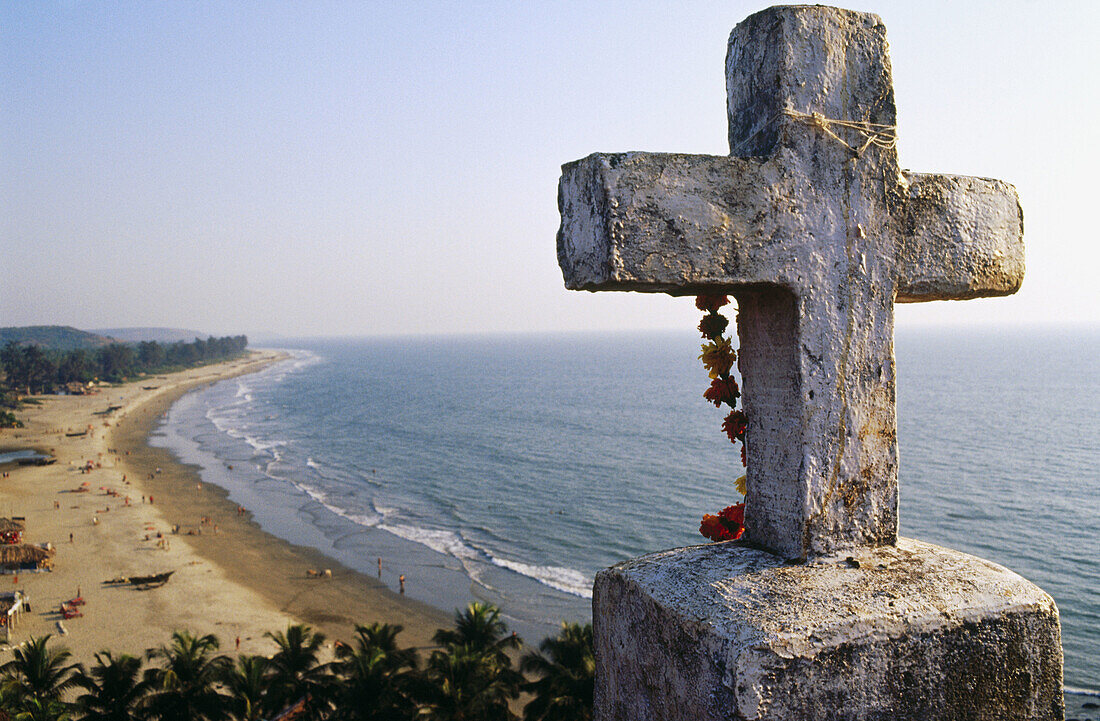 Cross and flowering offers with Arambol beach in background. Goa, India