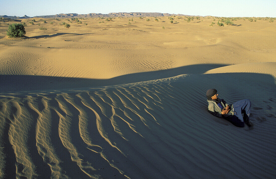 A Moroccon Arab rests at a stretch of sand dunes near the palmery of Oulad Driss. Drâa valley, southern Morocco.