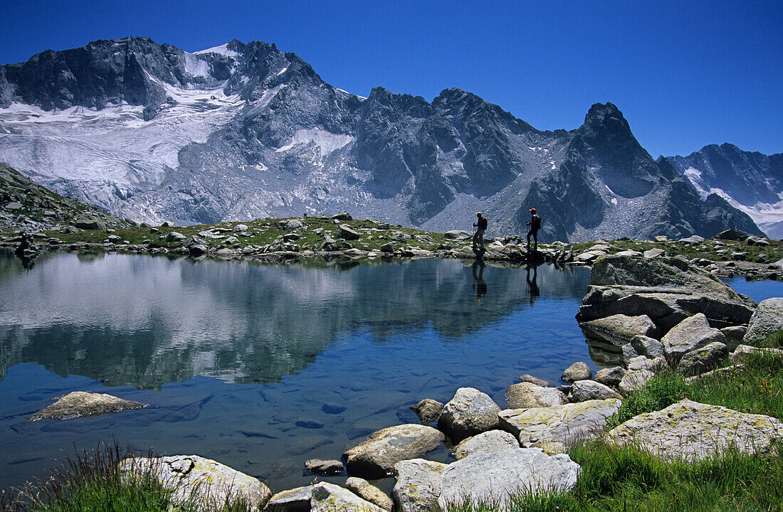 Zwei Wanderer am Ufer eines Sees, Cima di Cantone spiegelt sich, Bergell, Graubünden, Schweiz