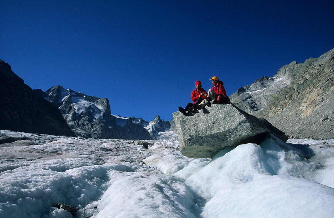 junges Pärchen sitzend auf Felsblock auf dem Fornogletscher, hinten Cima di Rosso, Bergell, Bregaglia, Graubünden, Schweiz