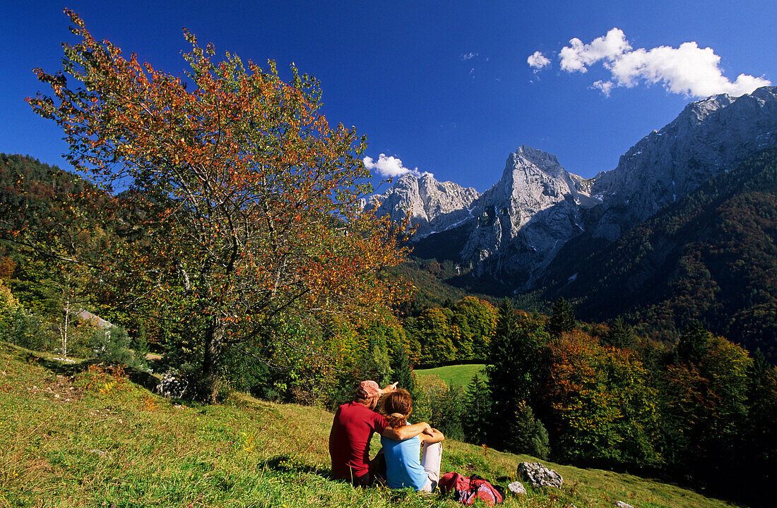 Paar sitzt auf Almwiese mit Blick Kaisergebirge, Wilder Kaiser, Tirol, Österreich