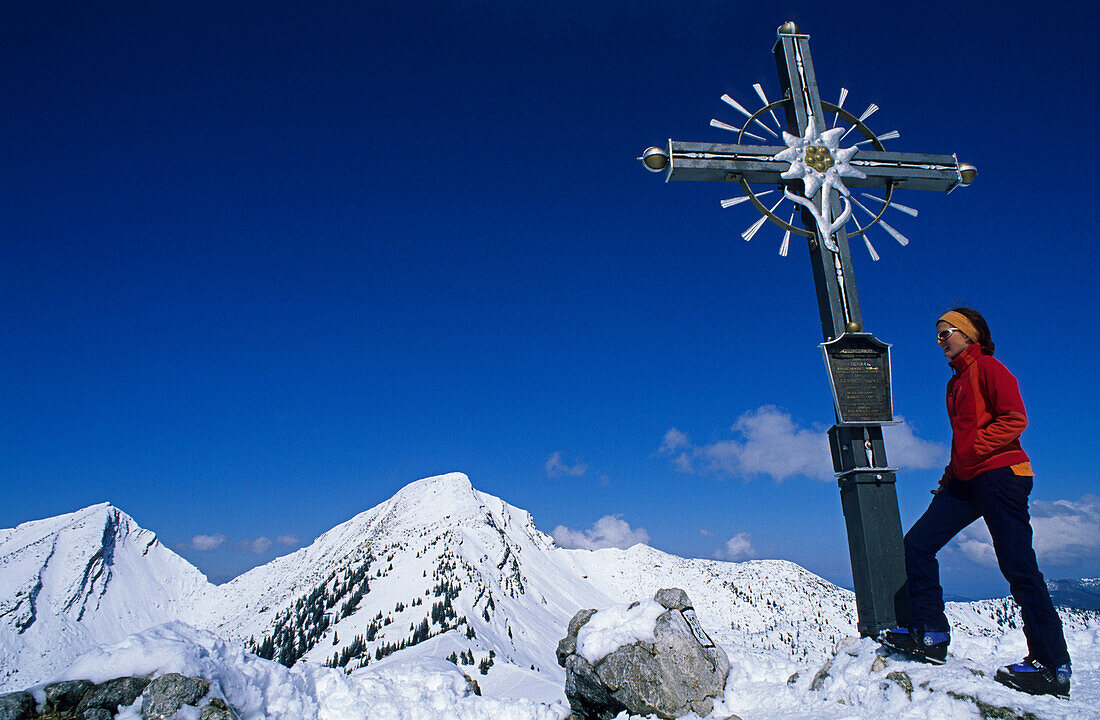 Woman at summit cross of mount Peitingkopfl, mountains Reifelberg and Sonntagshorn in background, Chiemgau range, Salzburg (state), Austria