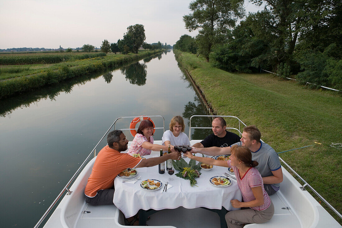 Freunde genießen Abendessen an Deck von Crown Blue Line Calypso Hausboot am Canal du Rhon au Rhin, nahe Eschau, Elsass, Frankreich, Europa