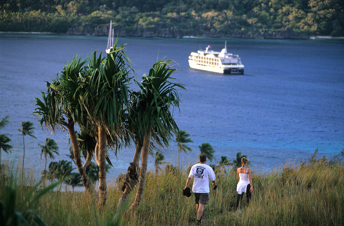 Ein Paar läuft entlang der Küste, Blaue Lagune mit MV Reef Escape vor Sawa-i-Lau, Yasawa Gruppe, Fidschi, Südsee