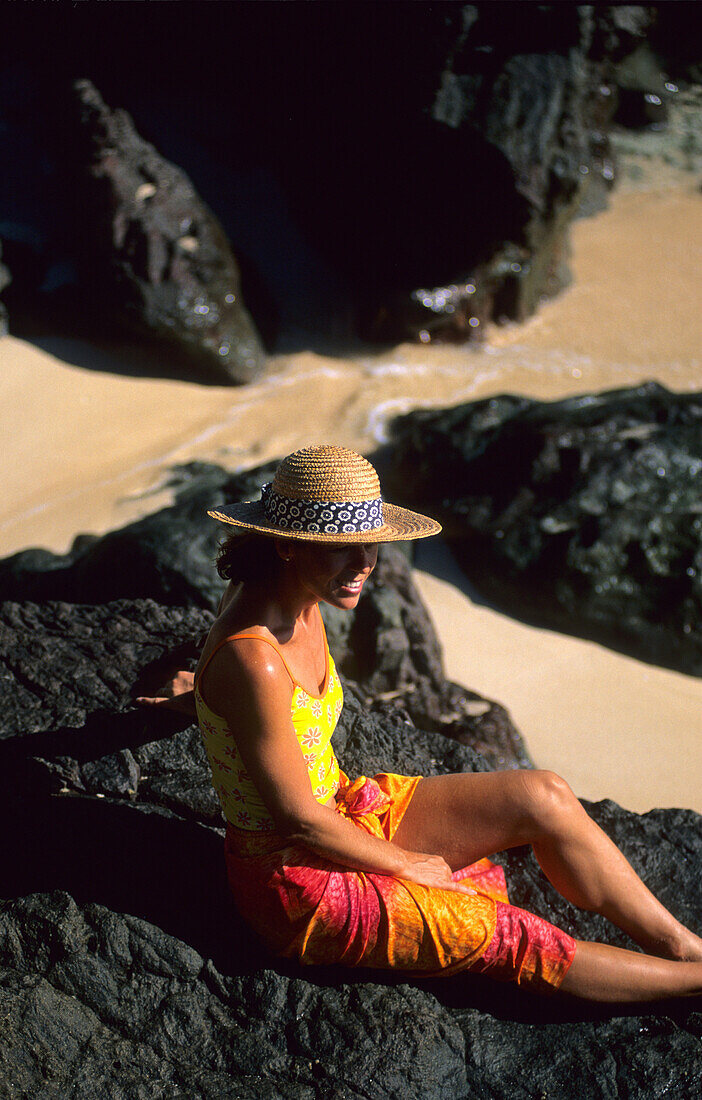 Frau sitzt auf Felsen am Strand und entspannt sich, Navadra Island, Mamanuca Gruppe, Fidschi, Südsee