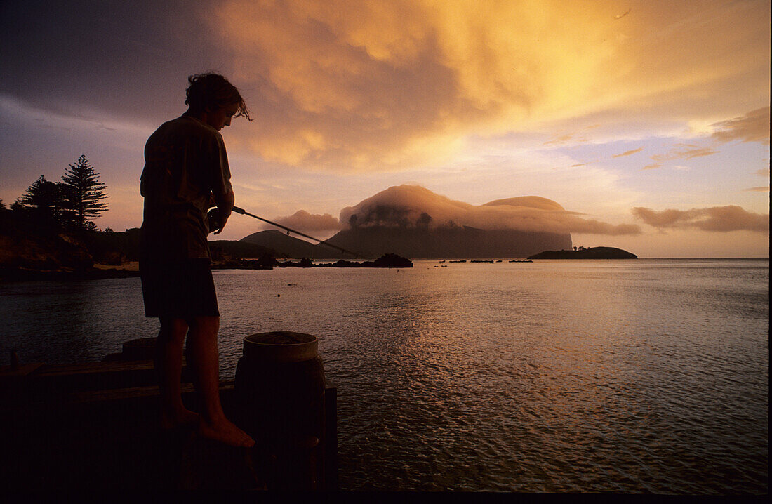 A man standing on landing stage fishing at sunset, Lord Howe Island, Australia