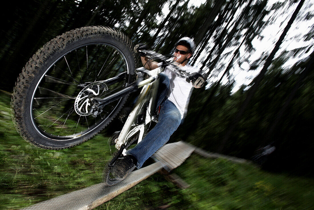 Mountainbiker fährt auf dem Hinterrad über einen Balken, Oberammergau, Bayern, Deutschland