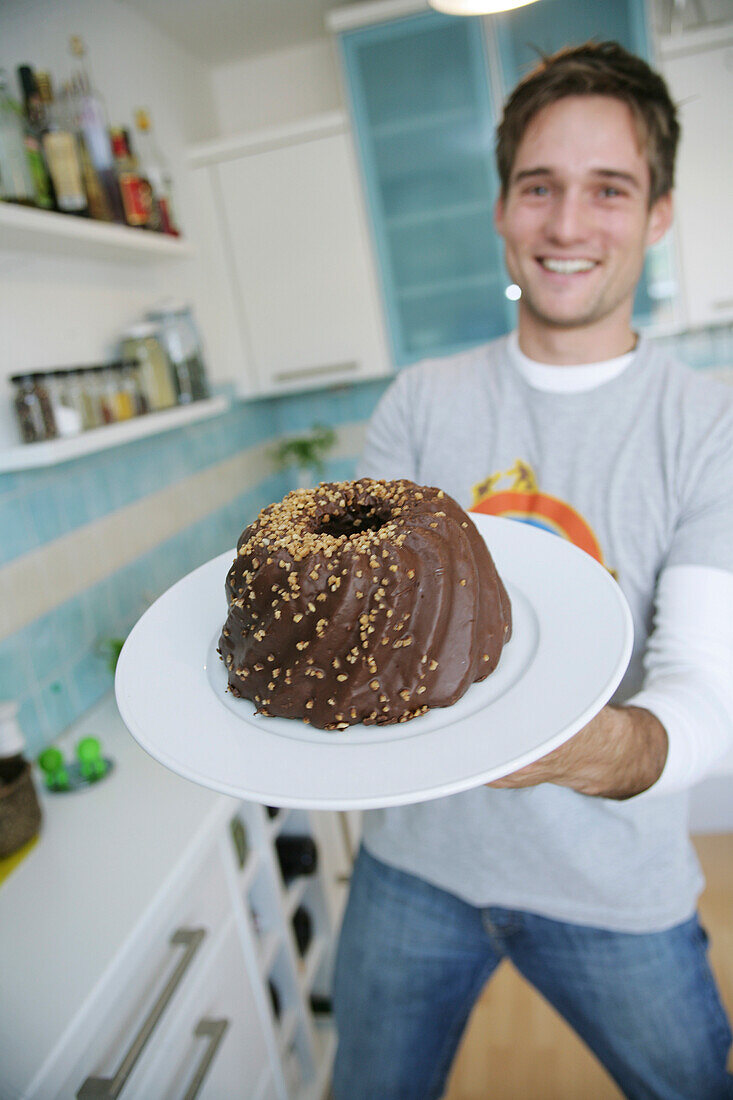 Junger Mann hält einen Schokoladenkuchen, München, Deutschland