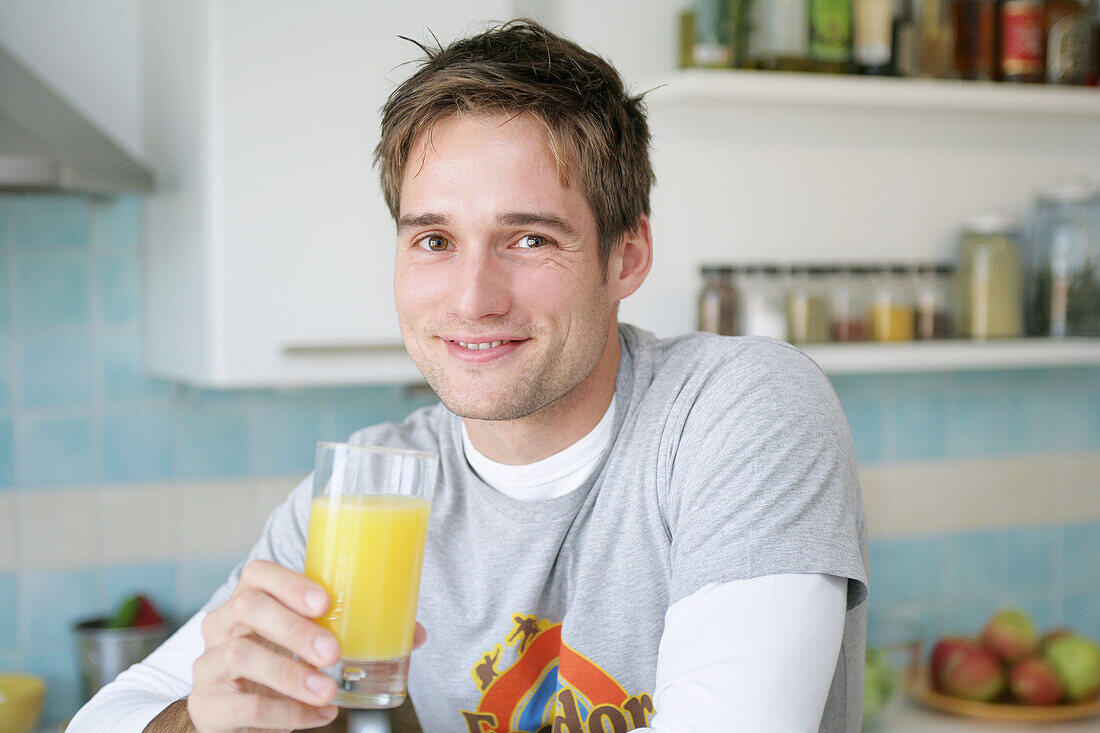 Young man holding a glass of orange juice, Munich, Germany