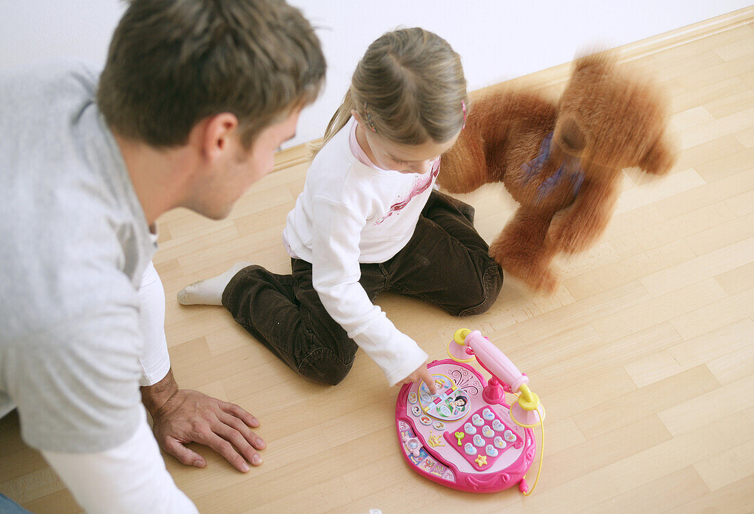 Father and daughter (3-4 years) playing with a toy phone and a teddy bear, Munich, Germany