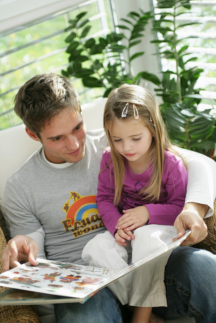 Father and daughter (3-4 years) reading a book, Munich, Germany