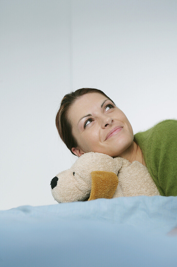 Junge Frau liegt mit Stoffhund auf Bett, München, Deutschland