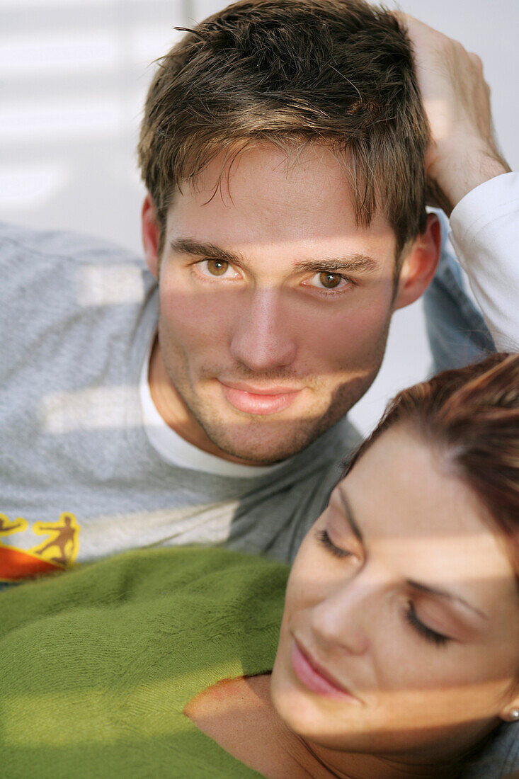Junger Mann blickt in die Kamera, junger Frau schläft im Vordergrund, München, Deutschland