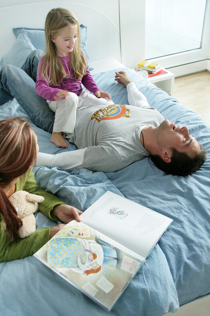 Junge Familie spielt auf einem Bett, München, Deutschland
