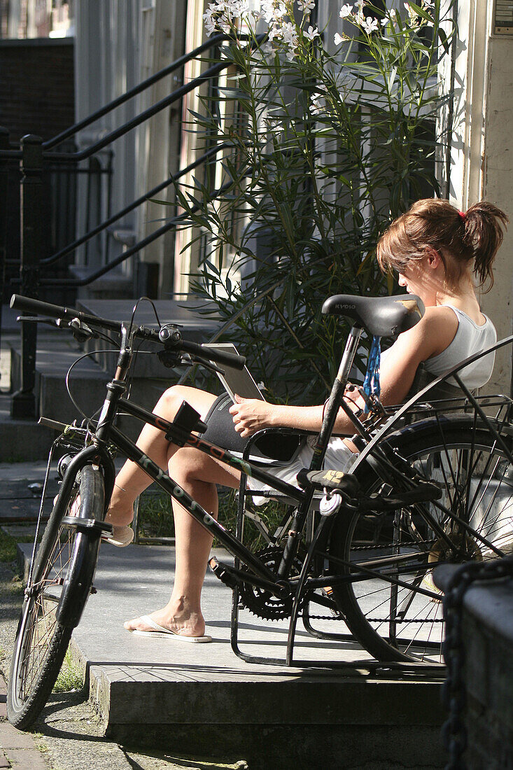 Woman with laptop sitting on bank, Oudezijds Voorburgwal, Amsterdam, Holland, Netherlands