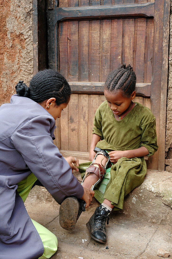 Health worker adjusting leg brace of a crippled girl in a slum of Addis Ababa, Ethiopia