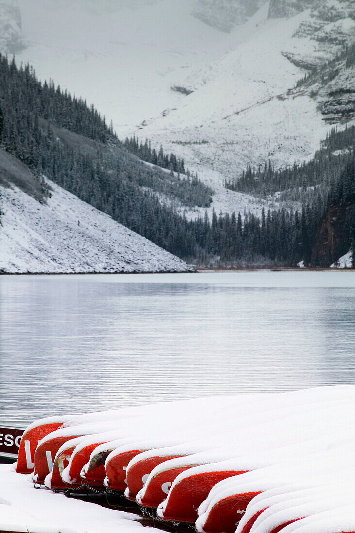 Red canoes under snow and lake in early winter. Lake Louise, Banff National Park. Alberta, Canada