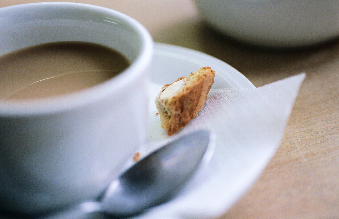 Partial view close-up of a white coffee cup and saucer with spoon and a piece of biscotti on the saucer