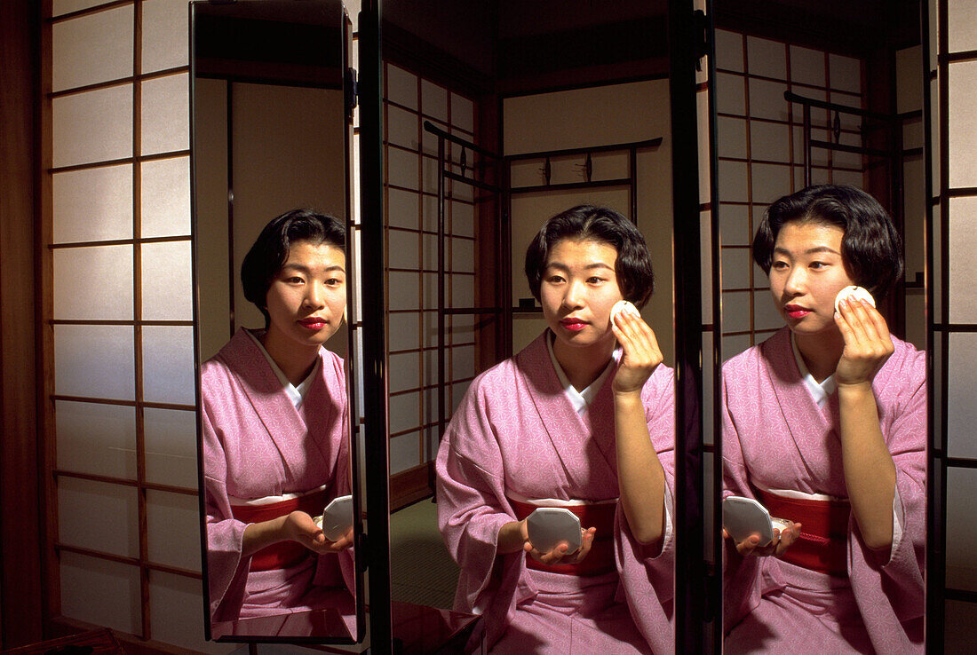 Japanese woman applies make up in a triple faced mirror in a Tokayo Hotel room. Japan