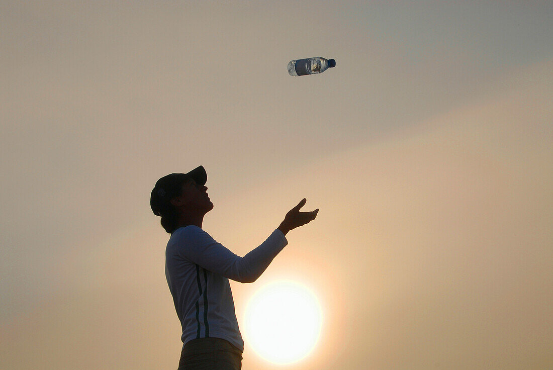 Woman throw a bottle of water up in the air, North Sea, Germany