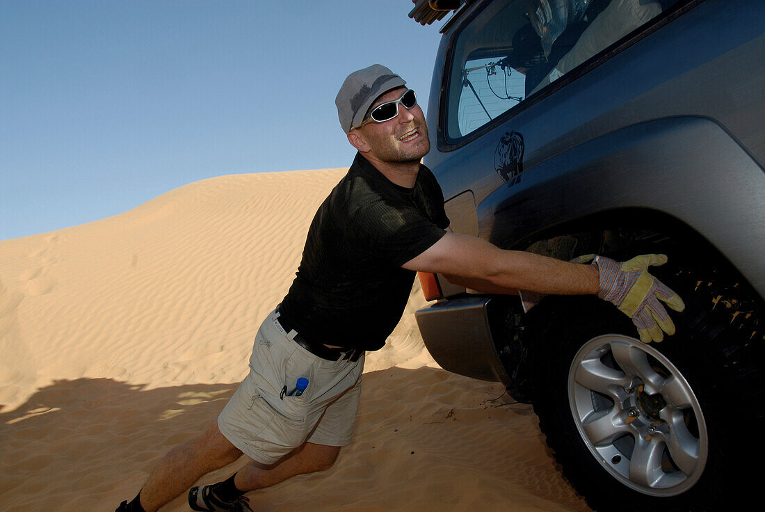 Man pushing a 4x4 vehicle, jeep out of the sand, Offroad 4x4 Sahara desert Tour, Bebel Tembain area, Sahara, Tunisia, Africa, mr