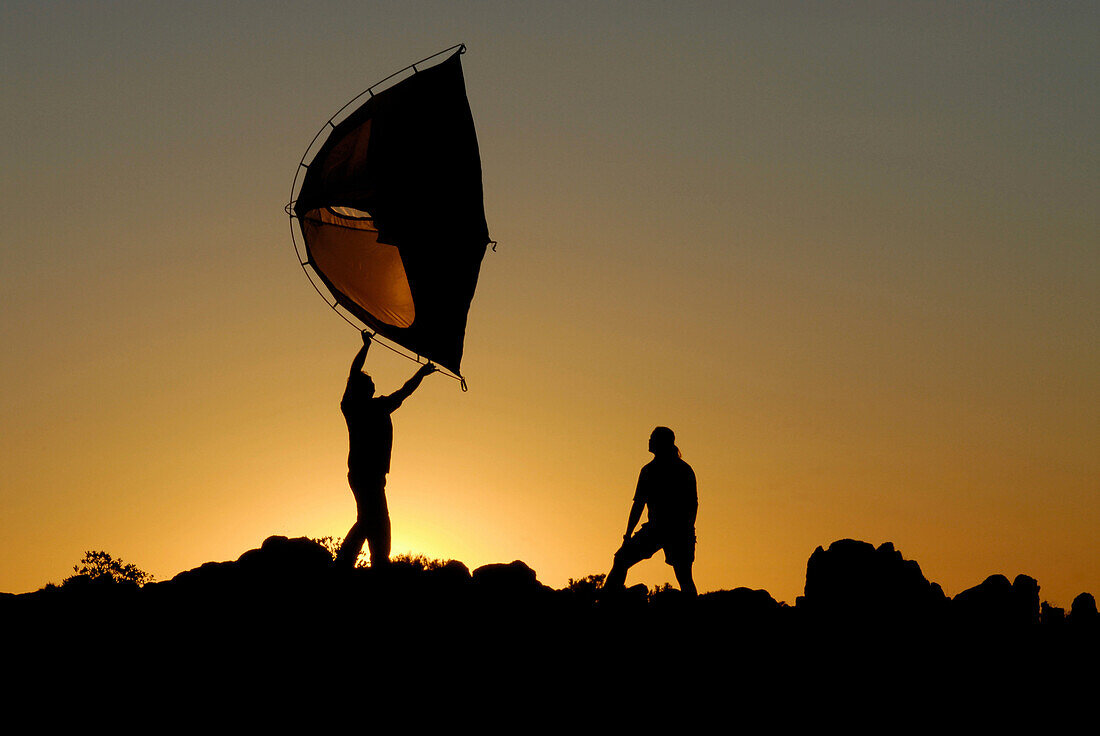 Two people putting up a tent in the sunset, camping, Sardegna, Sardinia,  Italy, Europe, mr