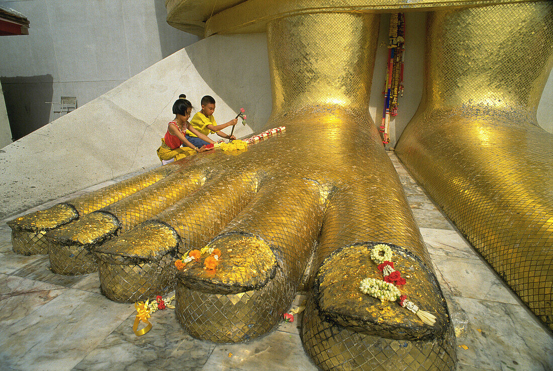 Two children place flower offering at feet of giant statute of Budda at Wat Intraviharn. bangkok. Thailand