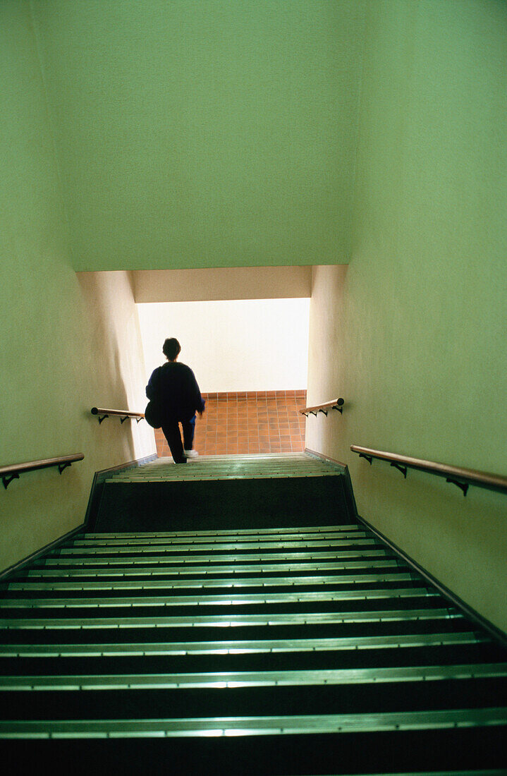 Single silhouetted figure of a woman at the bottom of a long and wide staircase