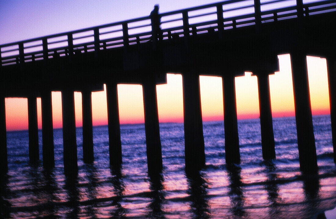 Silhouette of the fishing pier at sunset at Coney Island. New York. A lone figure is on the walkway