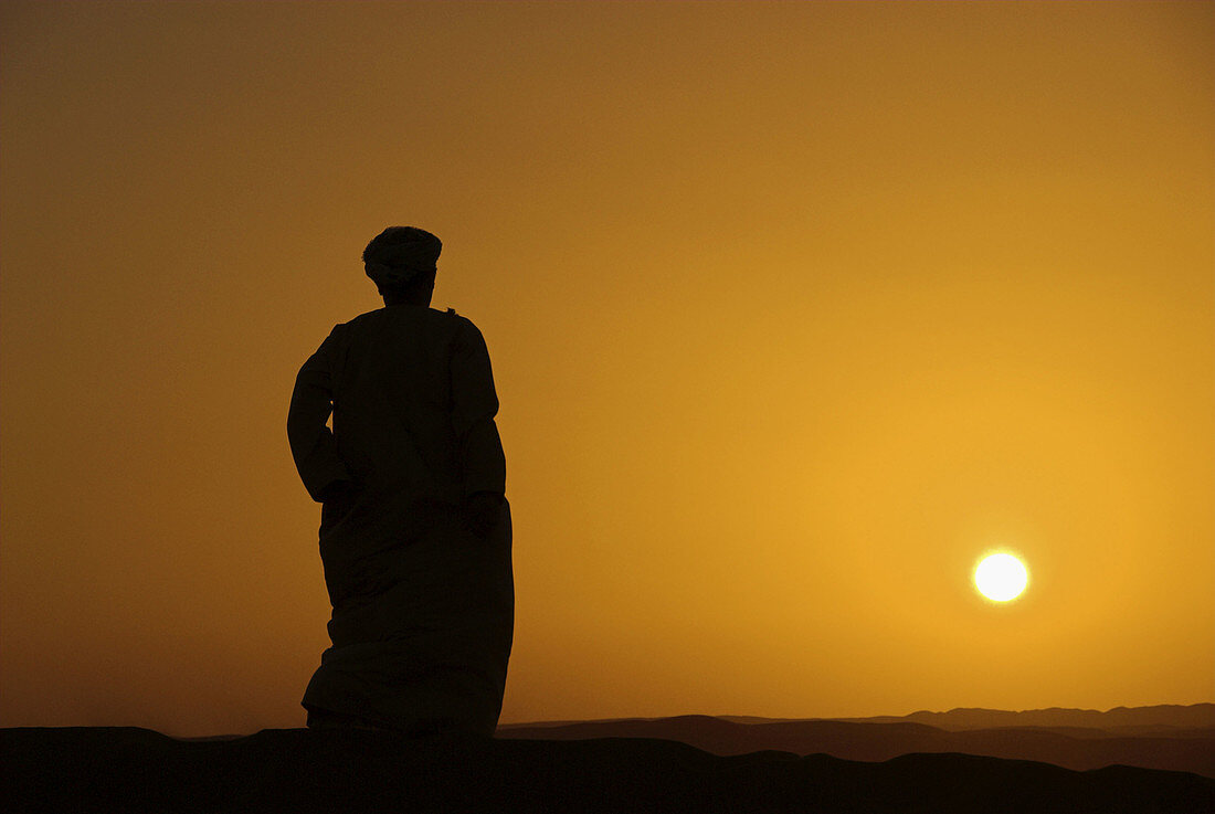 Omani man on the dunes, watching the sunset, northern edge of the Wahiba Sands, Oman
