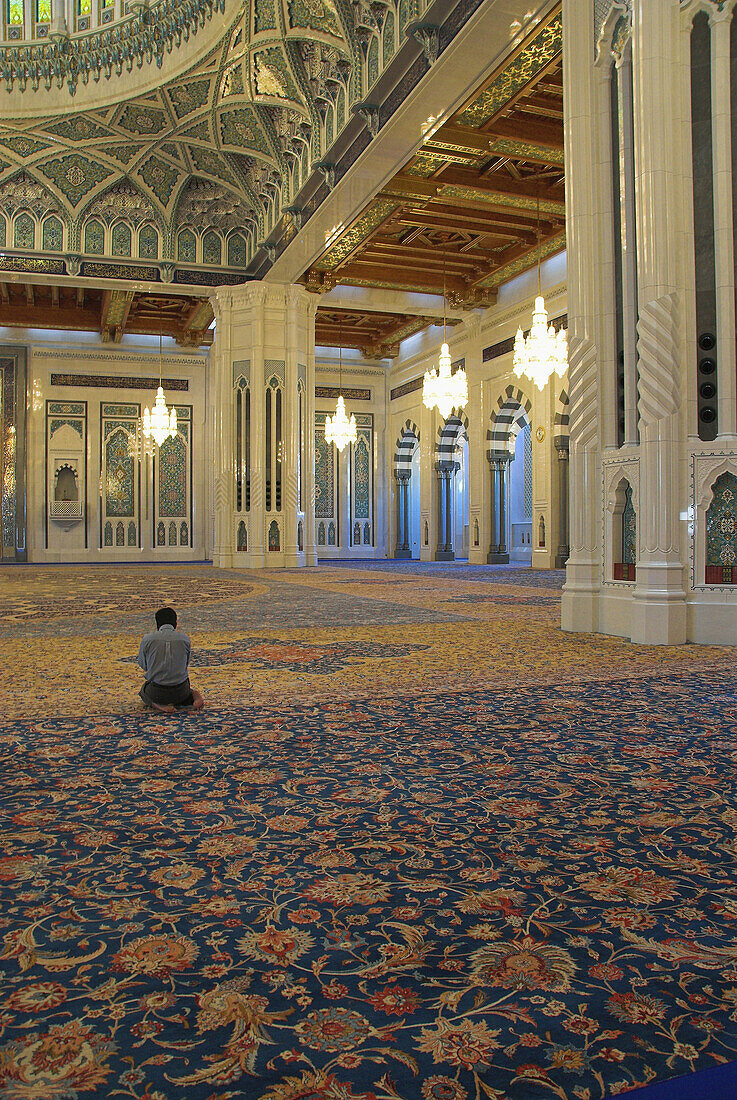 Lone muslim praying, kneeling on the world s largest single carpet, in the main hall of the Sultan Qaboos Grand Mosque, Muscat, Oman