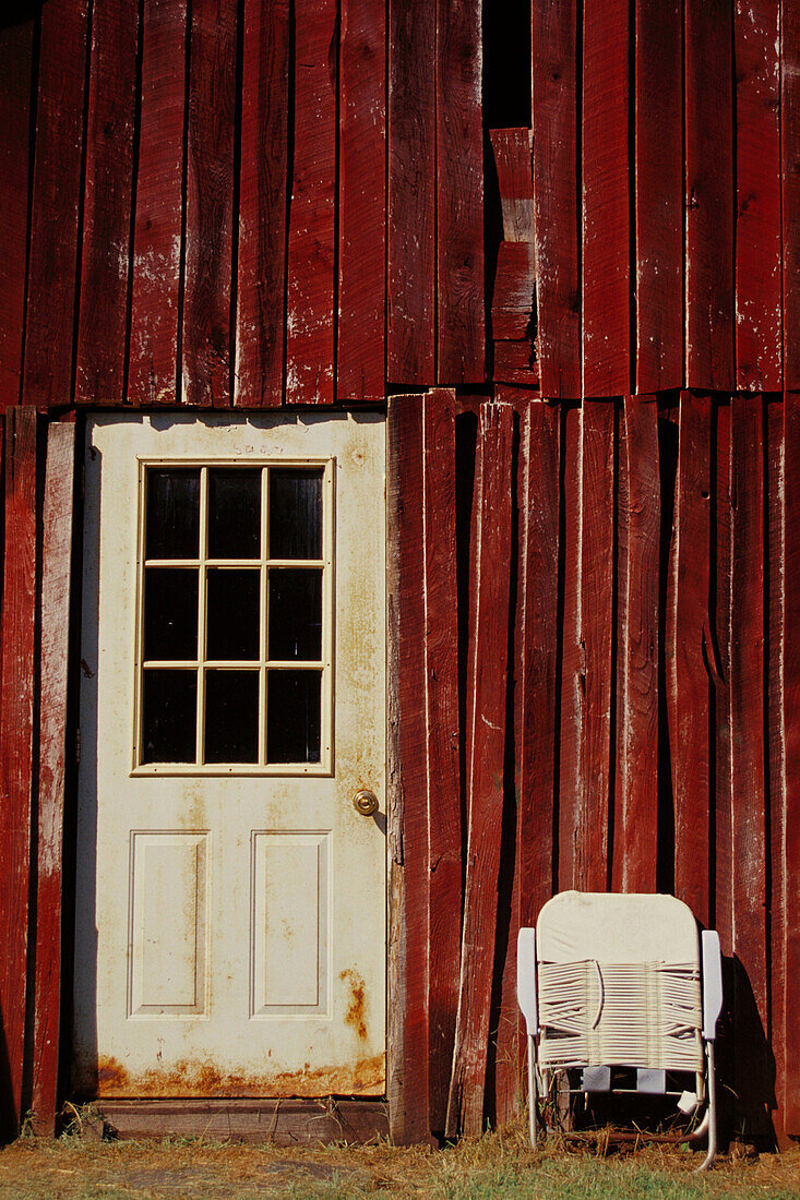 Red-brown side of barn with white painted door and folded white lawn chair, Unionville, Indiana, USA