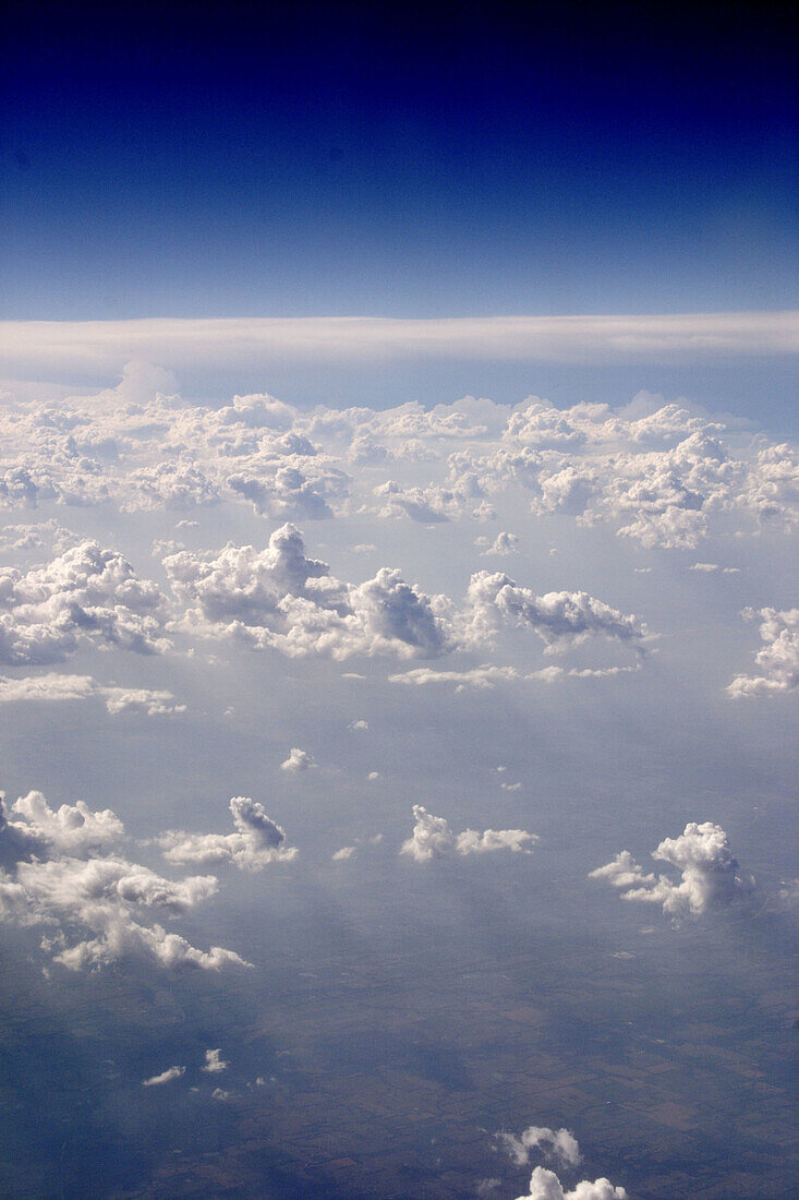 ranks of clouds seen from jet airplane, with blue sky deepening to near-black, landscape faintly visible below clouds