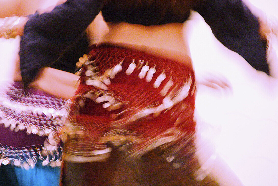 torso and arms of belly dancer, blurred with motion, another dancer s torso partially visible in background