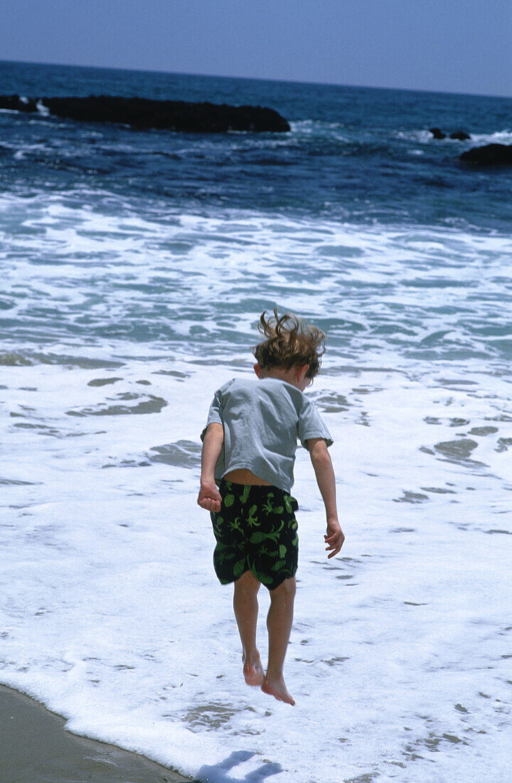 Caucasians, Child, Childhood, Children, Coast, Coastal, Color, Colour, Daytime, Exterior, Foam, Foamy, Froth, Human, Jump, Jumping, Jumps, Kid, Kids, Leisure, Male, Motion, Movement, Moving, North Ame