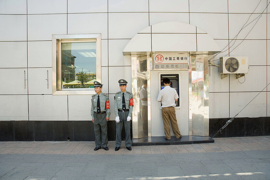 Wang Fu Jing road, people passing by, cash teller, policemen. Beijing. China.