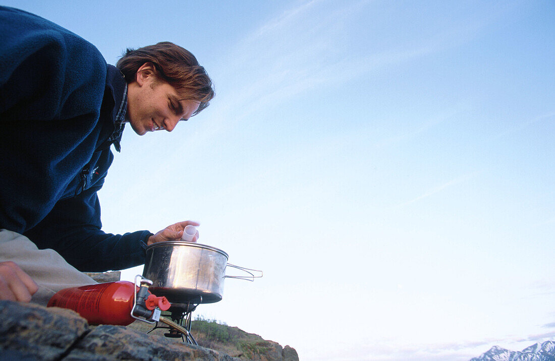 Man cooking meal on stove. Chugach State Park. Southcentral Alaska