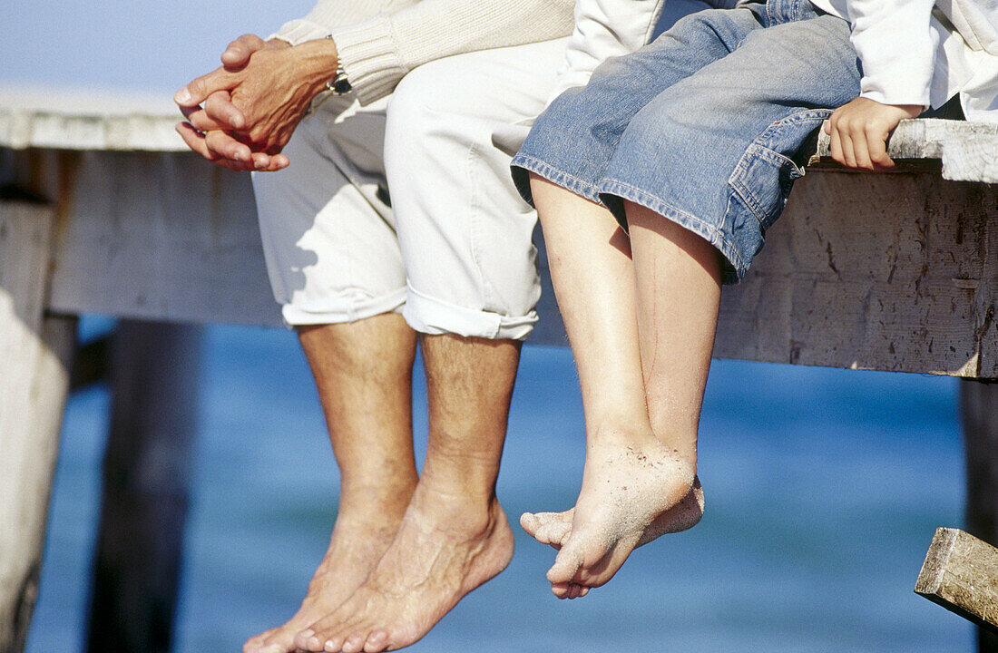 Vater und Kind sitzen auf einem Holzsteg über dem Meer