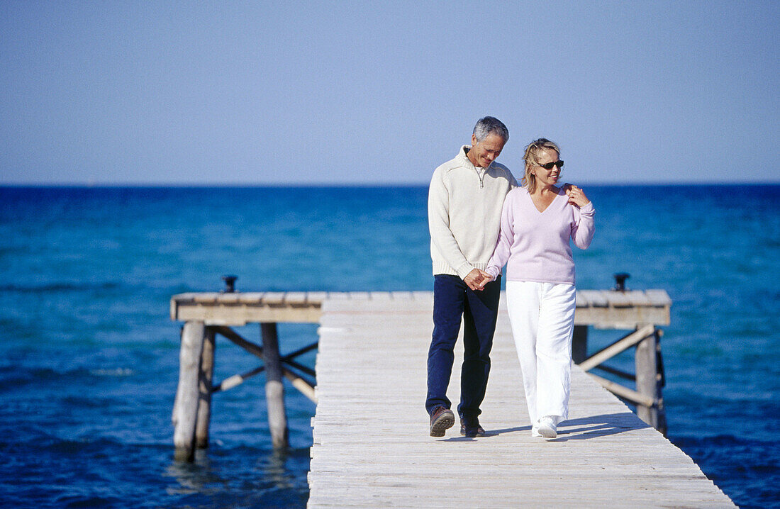 Couple walking in a wooden footbridge over the sea