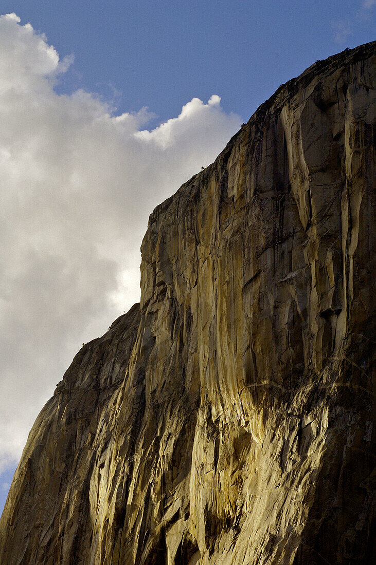 Blue sky, clouds, and sunlight on sheer granite cliff face wall of El Capitan, Yosemite Valley, Yosemite National Park, California