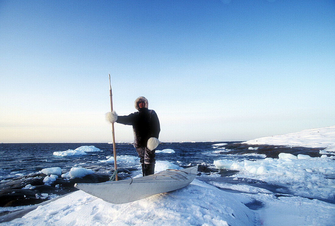 Esquimo hunter standing on pack ice besides canoe. Greenland