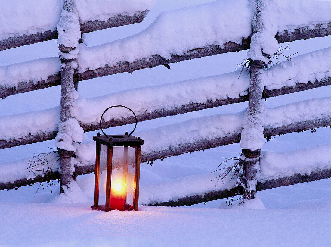 Lantern with candle in front of snow-covered fence. Skelleftea, Västerbotten, Sweden