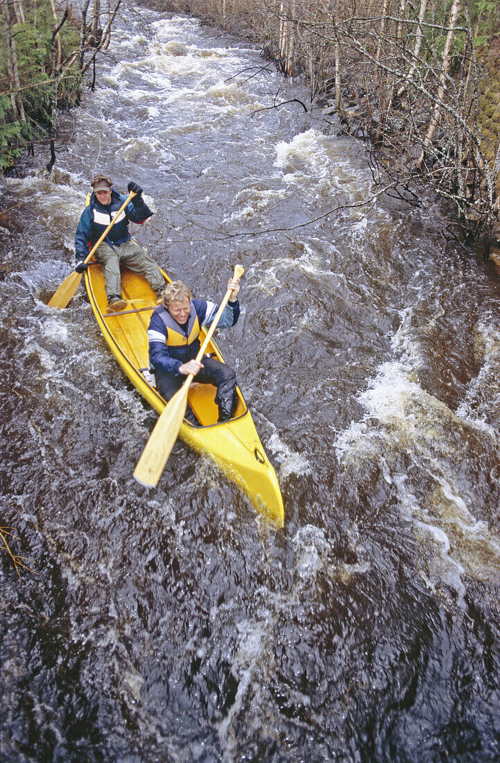 Two men paddling a canoe in a streamy river in spring. Klintforsliden, Vasterbotten. Sweden.