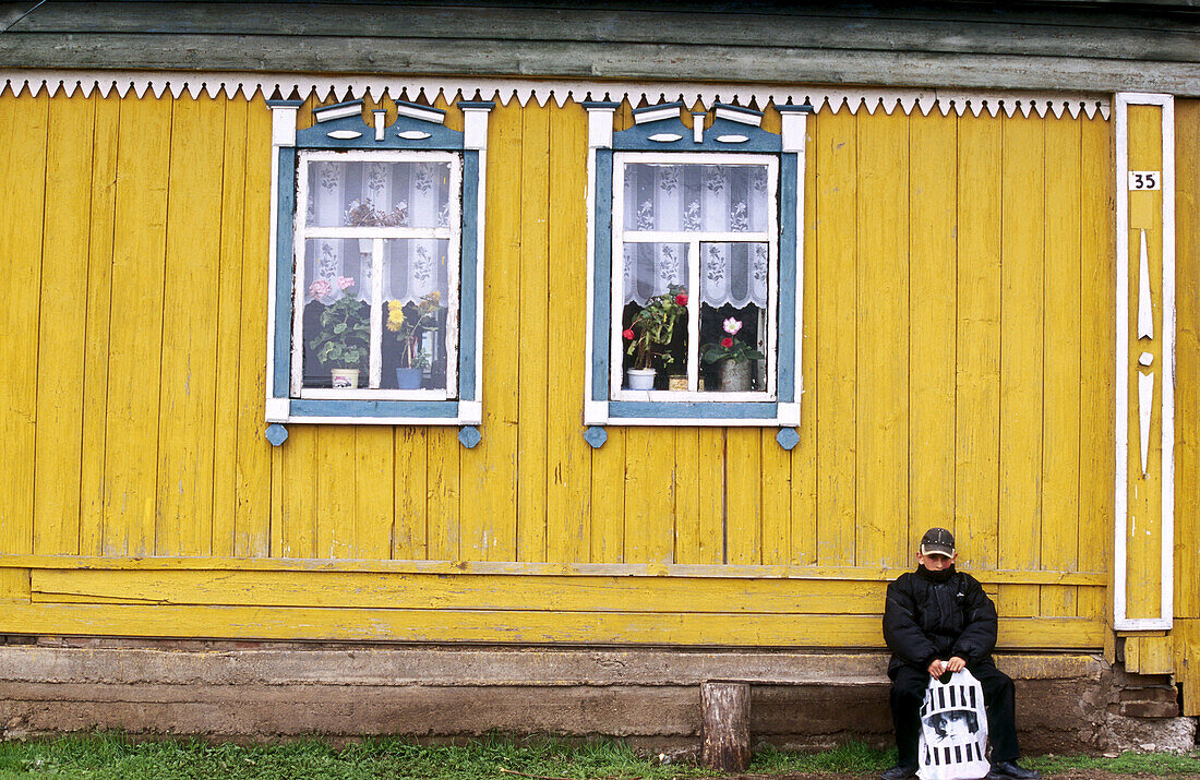 A yellow house with two windows and a boy waiting for the bus. Near Ufa. Bashkortostan. Russia.