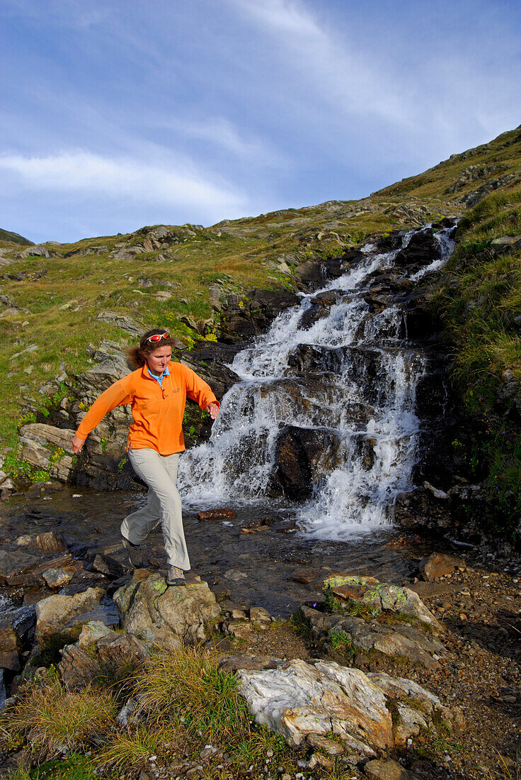 young woman jumping over stream, Lago del Naret (Lago del Narèt), Ticino, Switzerland