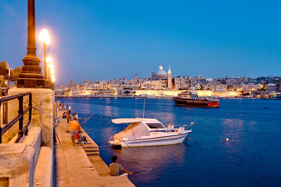 Angler sitzen am Abend auf der Uferpromenade, Blick auf die Stadt Valletta, Sliema, Malta, Europa