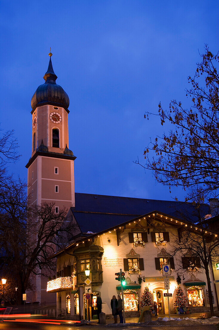 Christmassy decorated and illuminated house in the evening, church St. Martin in background, Garmisch, Garmisch-Partenkirchen, Germany